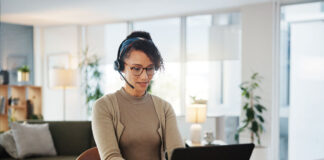 In Difficult Labor Market, Employers Turn to Remote Staffing woman wearing headset works at laptop computer in living room remote staffing VAs housing real estate