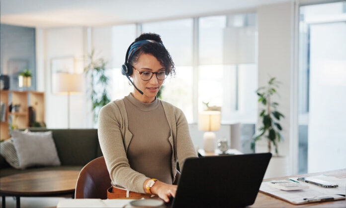 woman wearing headset works at laptop computer in living room remote staffing VAs housing real estate